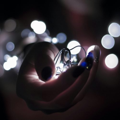 Close-up of a hand holding glowing string lights with a bokeh effect, creating a festive atmosphere.